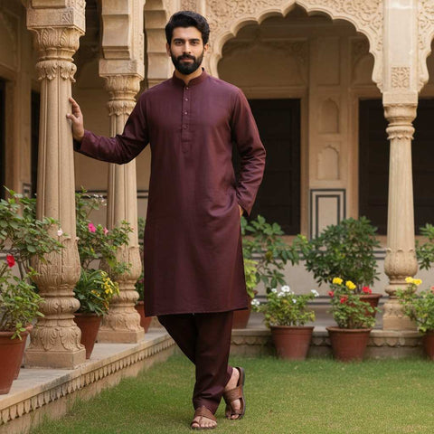 Man in a maroon kurta standing in an ornate outdoor setting with plants and flowers.