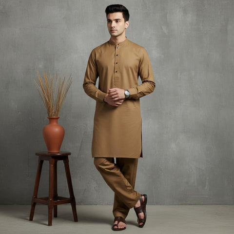 Man wearing a brown kurta standing next to a wooden stool with a vase against a gray wall.