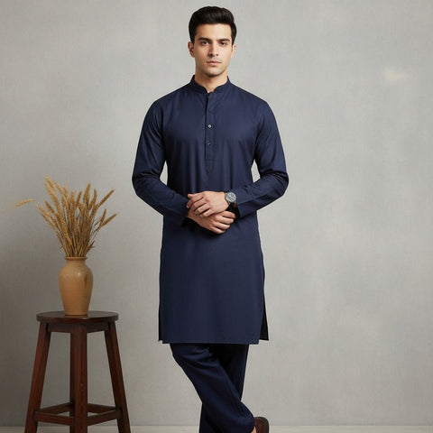 Man wearing a navy kurta standing next to a wooden stool with a vase on it against a plain background