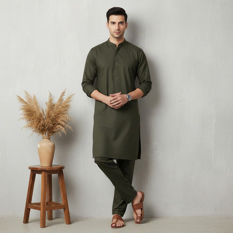 Man wearing a green kurta standing next to a wooden stool with decorative plants against a plain background