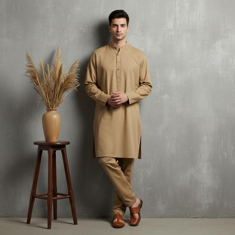 Man wearing a beige kurta standing next to a wooden stool with a vase of dried plants against a gray wall.