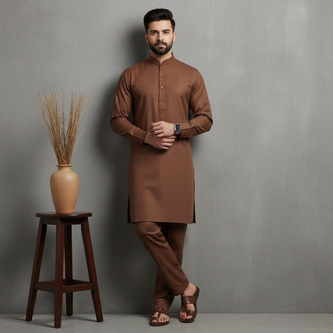 Man wearing a brown kurta standing next to a wooden stool with a vase against a gray background