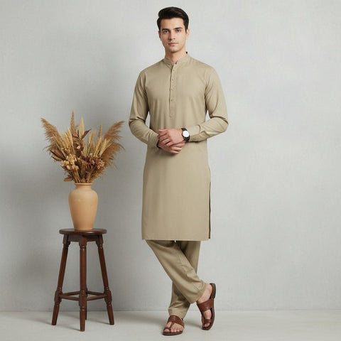 Man wearing a beige kurta with pants standing next to a wooden stool with a vase of dried plants on a light gray background