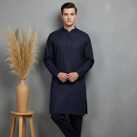 Man wearing a navy kurta standing next to a vase with dried plants on a gray background