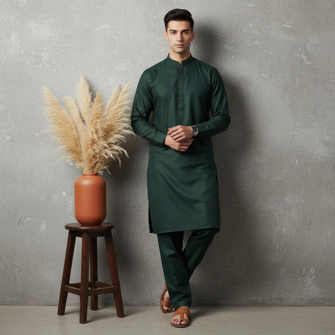 Man wearing a green kurta standing next to a vase with dried plants against a gray wall.