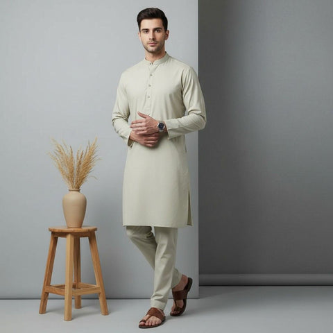 Man wearing a light green kurta with beige pants standing next to a wooden stool with a vase.