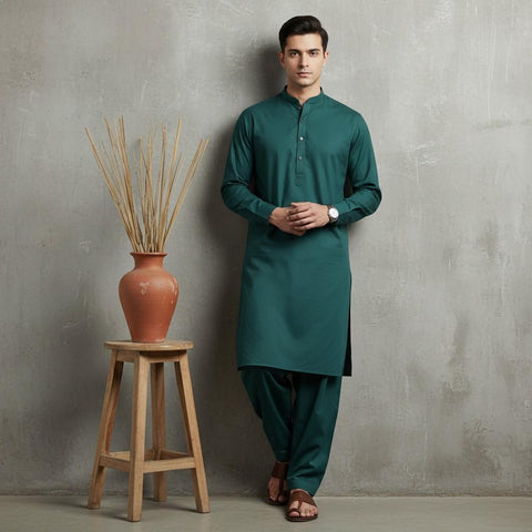 Man wearing a green kurta standing next to a wooden stool with a vase against a gray wall.